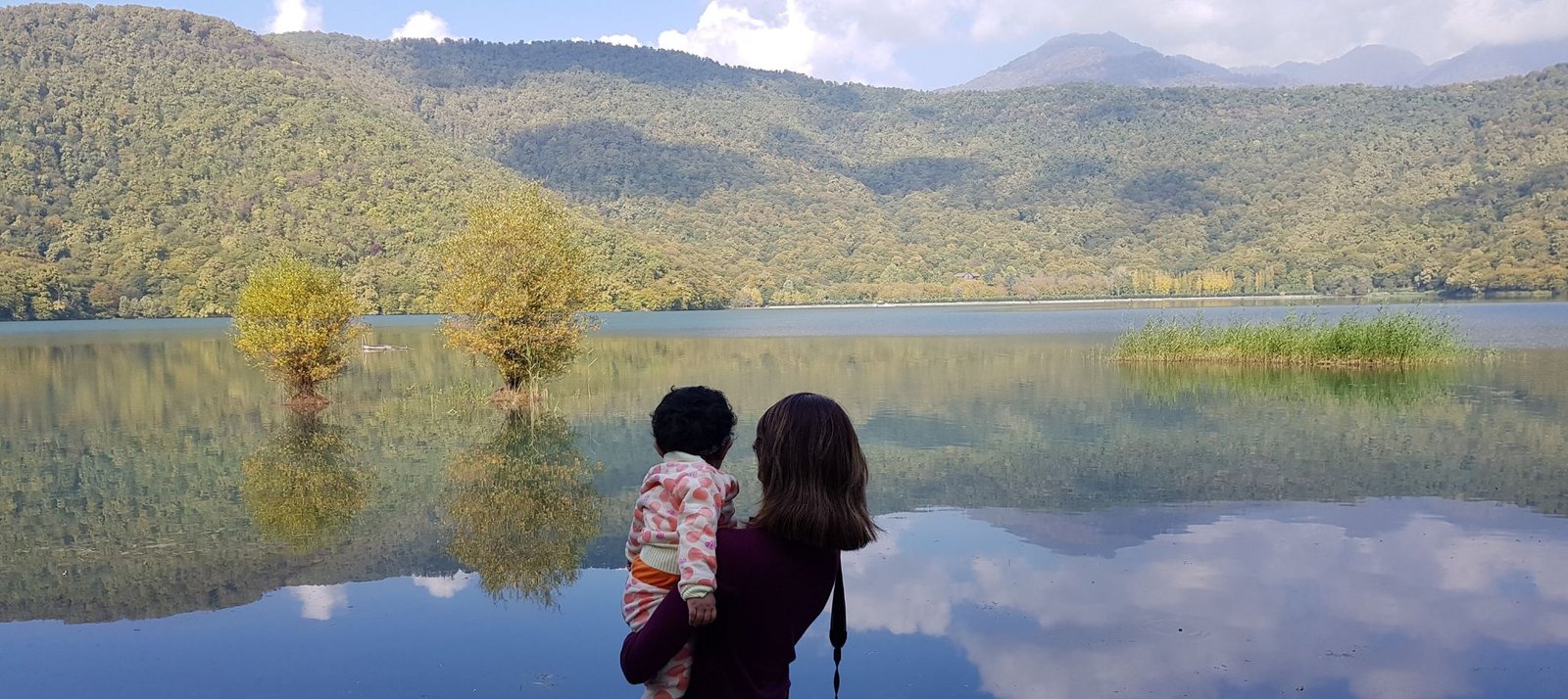 Mother holding daughter in arms near a lake and mountain view