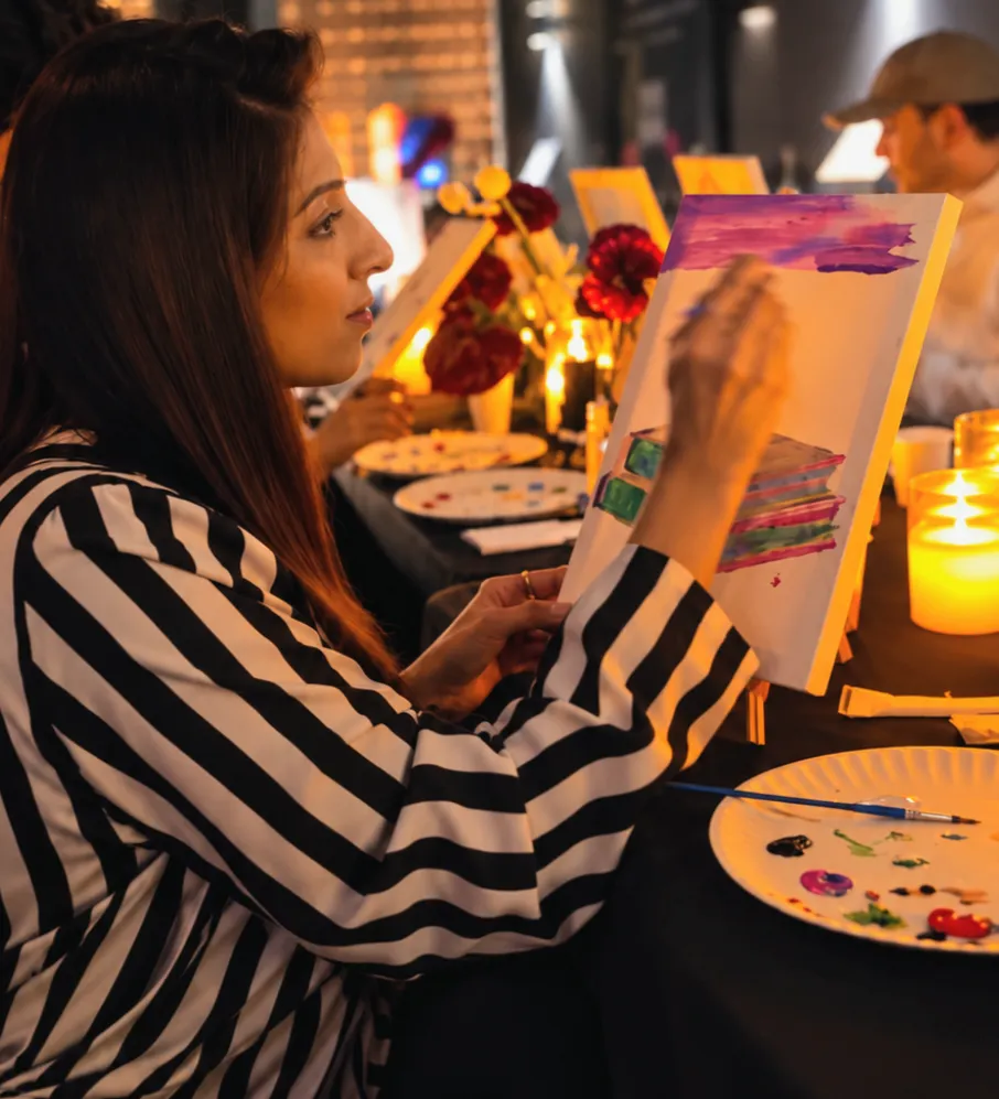 Suman Shafi painting a colourful canvas at a candlelit murder mystery paint workshop.